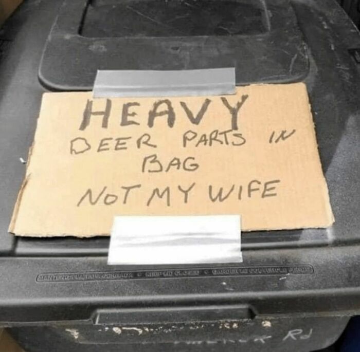 Cardboard sign with funny stupid message about heavy deer parts in a bag, taped to a black trash bin lid.
