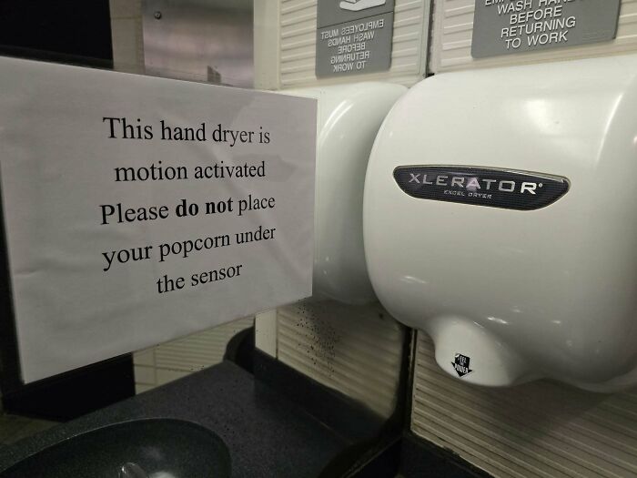 Hand dryer with a humorous sign warning not to place popcorn under the motion-activated sensor, funny stupid signs pic.