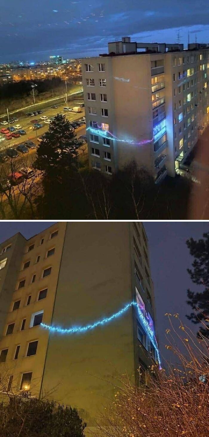 Festive Christmas lights strung between windows across a tall Eastern European apartment building at night.