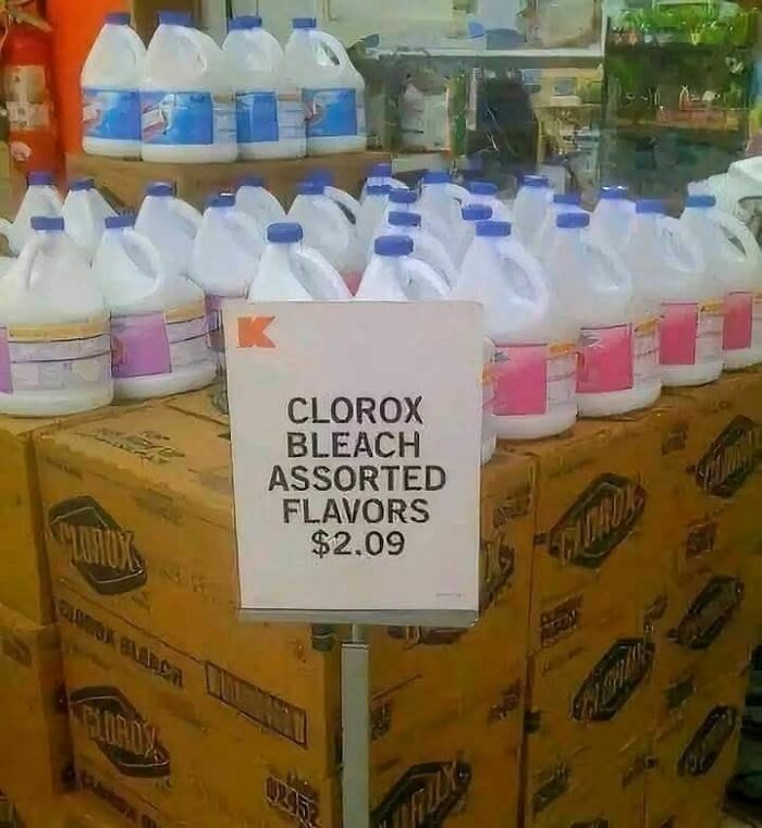 Display of bleach bottles with a sign humorously labeling them as assorted flavors at a grocery store.