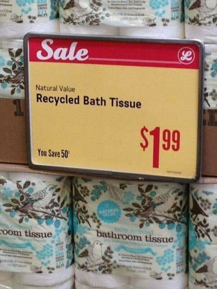 Sale sign for recycled bath tissue priced at $1.99 displayed above bathroom tissue rolls in a store shelf.