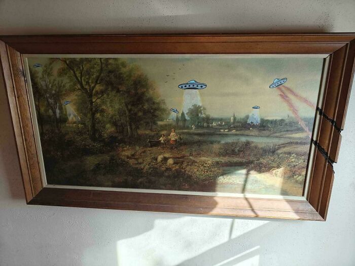 Thrifted painting of a countryside scene humorously altered with UFOs beaming light in a playful unexpected twist.