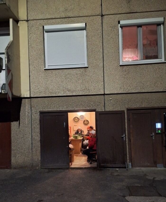 Group of people drinking inside a small garage, illustrating Eastern Europe humor and everyday life scenes.
