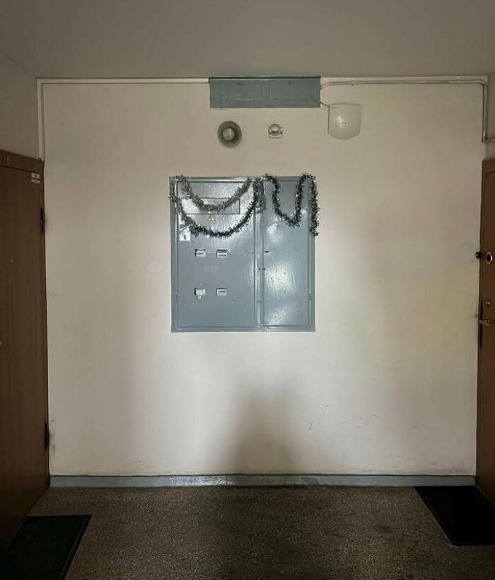 Eastern Europe apartment hallway with tinsel decoration on electrical panel, typical old building interior humor meme.