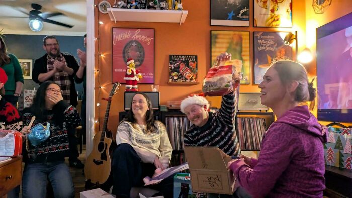Group of people celebrating with quirky and bizarre Christmas gifts in a cozy festive living room setting.