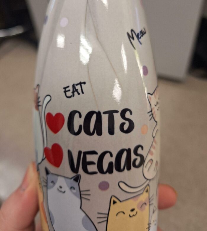 Close-up of a bizarre Christmas gift bottle with cartoon cats and text saying eat cats Vegas, a strange holiday present idea.
