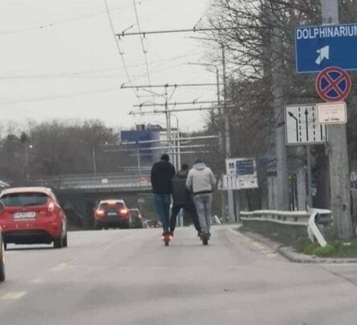 Three people on scooters riding on a road with cars and traffic signs, capturing Eastern Europe everyday moments.