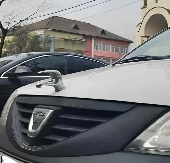 Close-up of a Dacia car with a water faucet hood ornament in an urban Eastern Europe setting, a funny relatable sight.