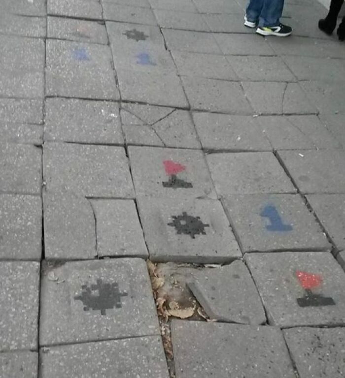 Worn and c*****d sidewalk tiles with faded painted game markings common in Eastern Europe streets.