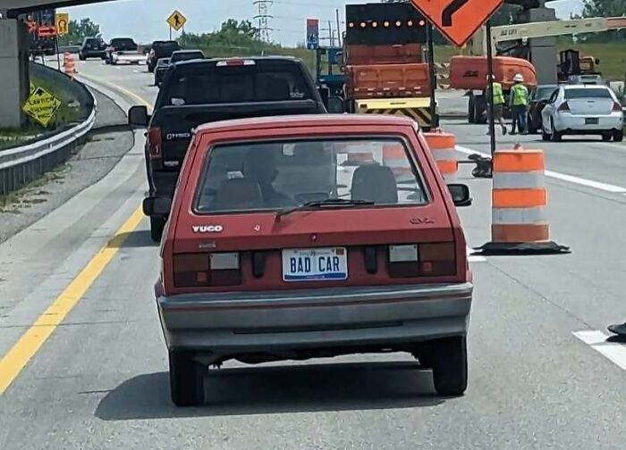 Red Yugo with BAD CAR license plate stuck in traffic near road construction, a relatable Eastern Europe meme.