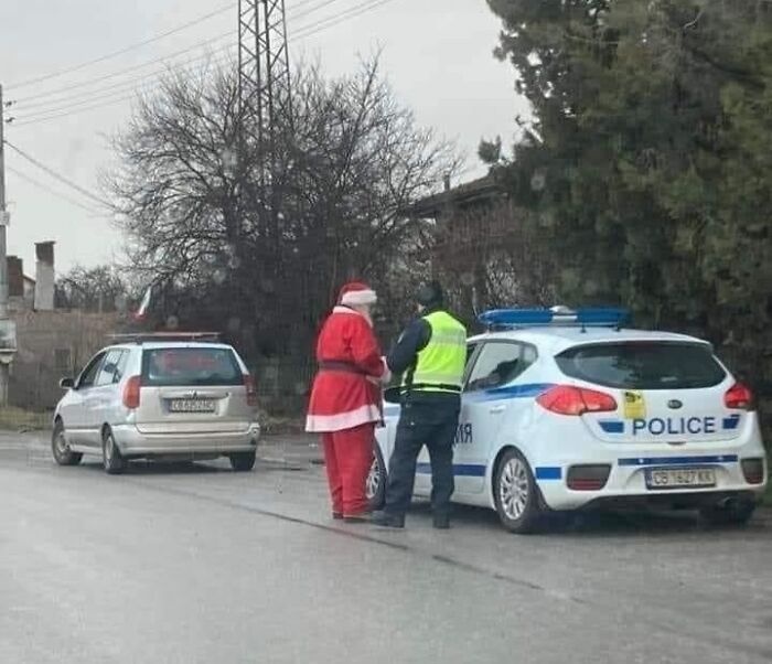 Police officer talking to a person dressed as Santa Claus next to a police car in an Eastern European street scene.