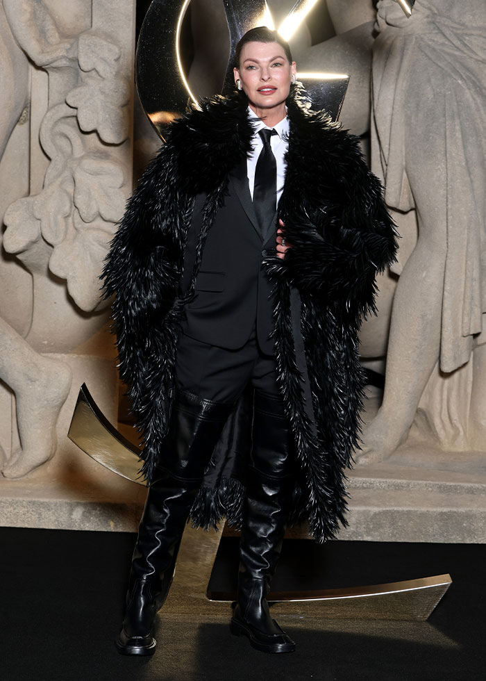 Celebrity fashion disaster in 2025 featuring an extravagant black fur coat, suit, and high leather boots at an event.