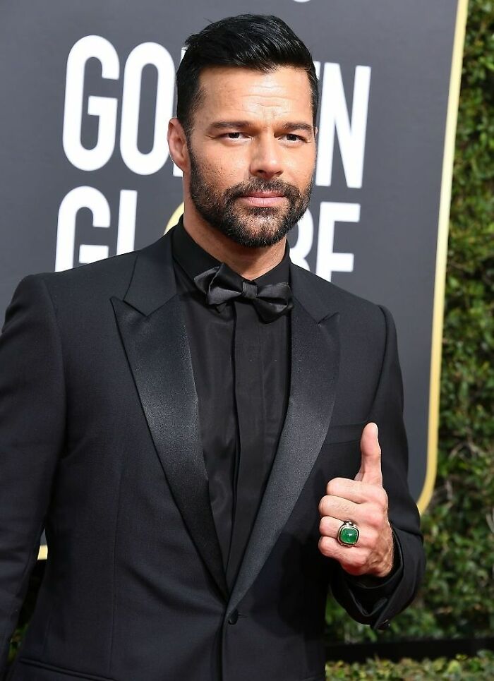 Ricky Martin in a black tuxedo giving a thumbs up at a formal event, highlighting his career as a singer and performer.