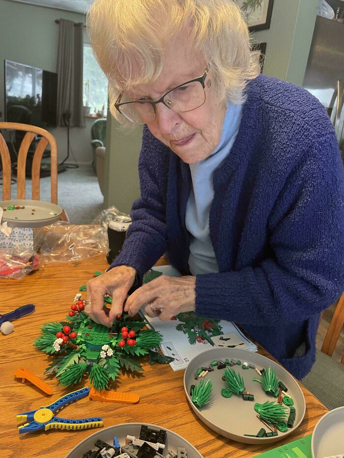 Elderly woman assembling a festive holiday wreath with greenery and red berries, creating sweet holiday moments at home.