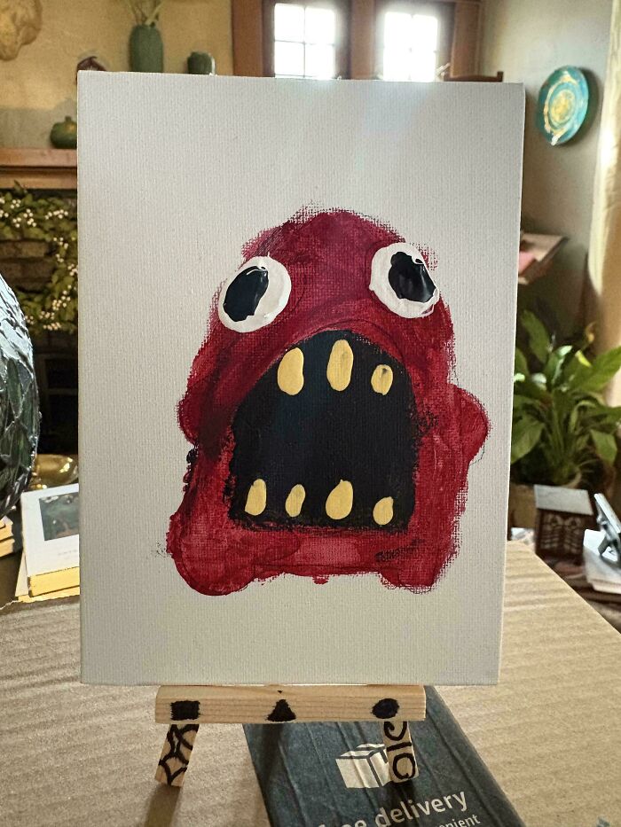 Abstract red monster painting with large eyes and teeth on a canvas displayed indoors during holiday moments.