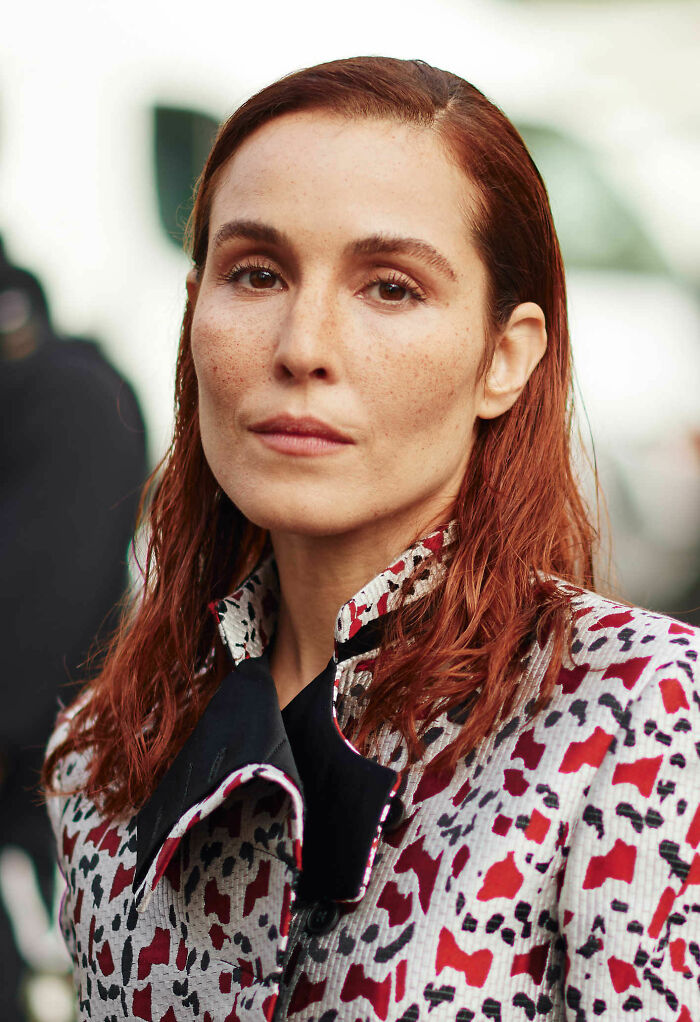 Noomi Rapace with red hair and patterned jacket, posing outdoors highlighting bio and career highlights.