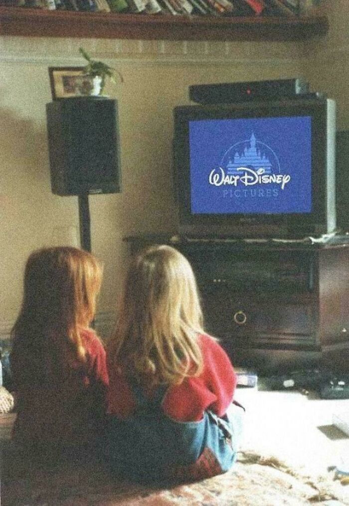 Two children sitting on the floor watching an old TV with Walt Disney Pictures logo, evoking 90s and 2000s nostalgia.