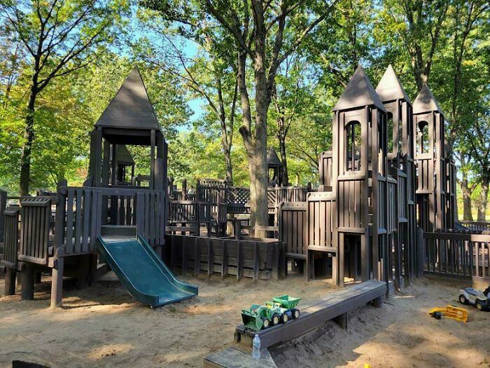 Wooden playground with slides and trucks under trees, evoking 90s and 2000s nostalgia and childhood memories outdoors.