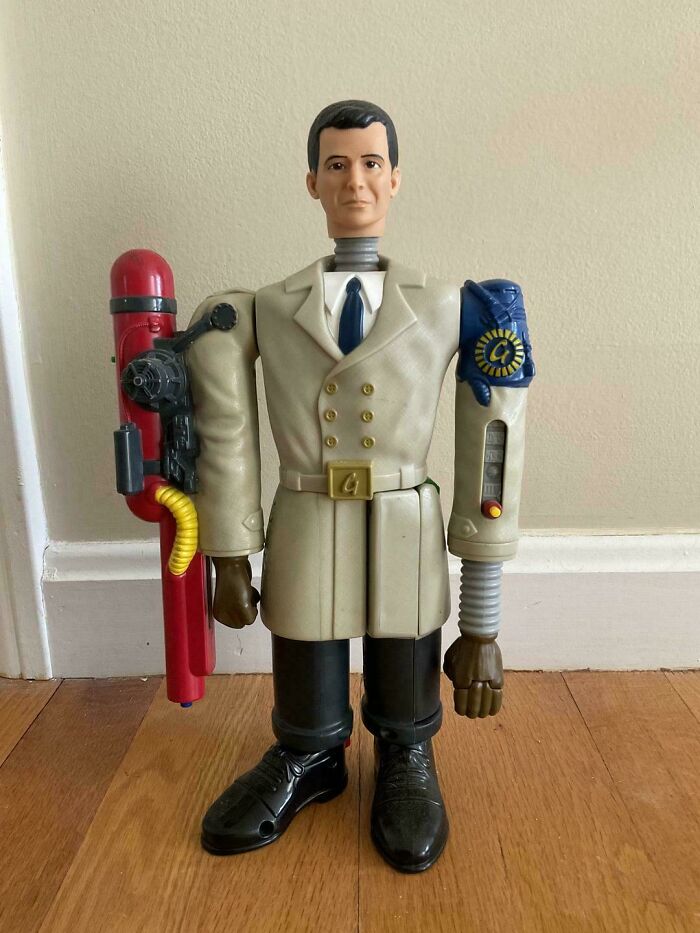 90s and 2000s nostalgia action figure toy with beige coat and mechanical arms standing on wooden floor indoors