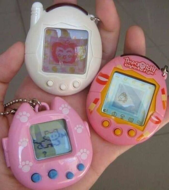 Three handheld digital pets from the 90s and 2000s nostalgia era displayed on a person's palm.