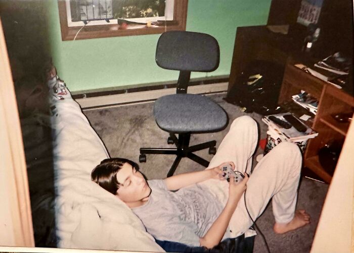 Teen playing video games on a couch in a 90s and 2000s nostalgia bedroom with vintage gaming console and accessories.