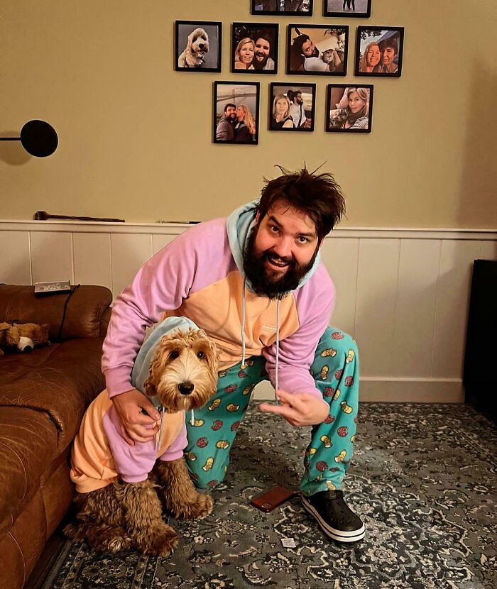 Man and dog wearing matching pastel hoodies and holiday-themed pants, sharing a sweet holiday moment indoors.