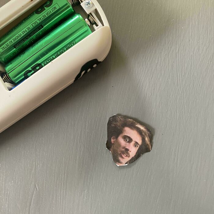 Small cutout of a surprised man's face placed on a gray surface next to a device with green batteries, showing sibling fun moments.