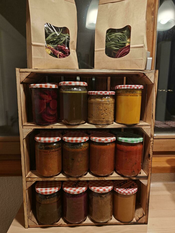Assorted homemade jars of preserves and two bags of dried herbs displayed on a wooden shelf for holiday moments.
