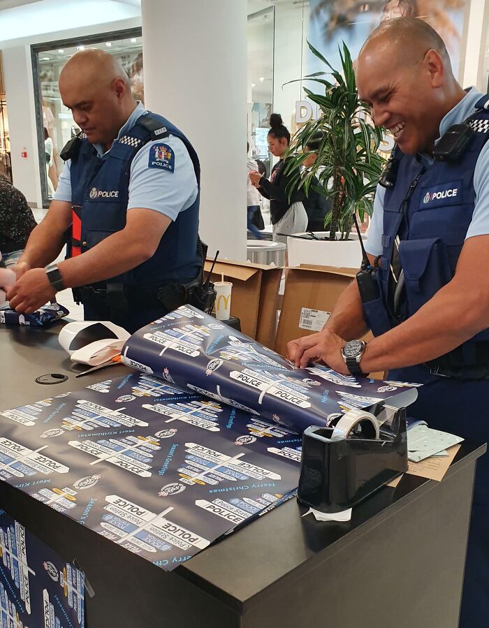 Two police officers wrapping holiday gifts at a mall, sharing sweet holiday moments that melt even the Grinchiest heart.