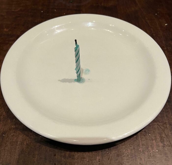 Single blue striped birthday candle burned down and stuck in an empty white plate, funny pictures capturing weirdness of 2025.