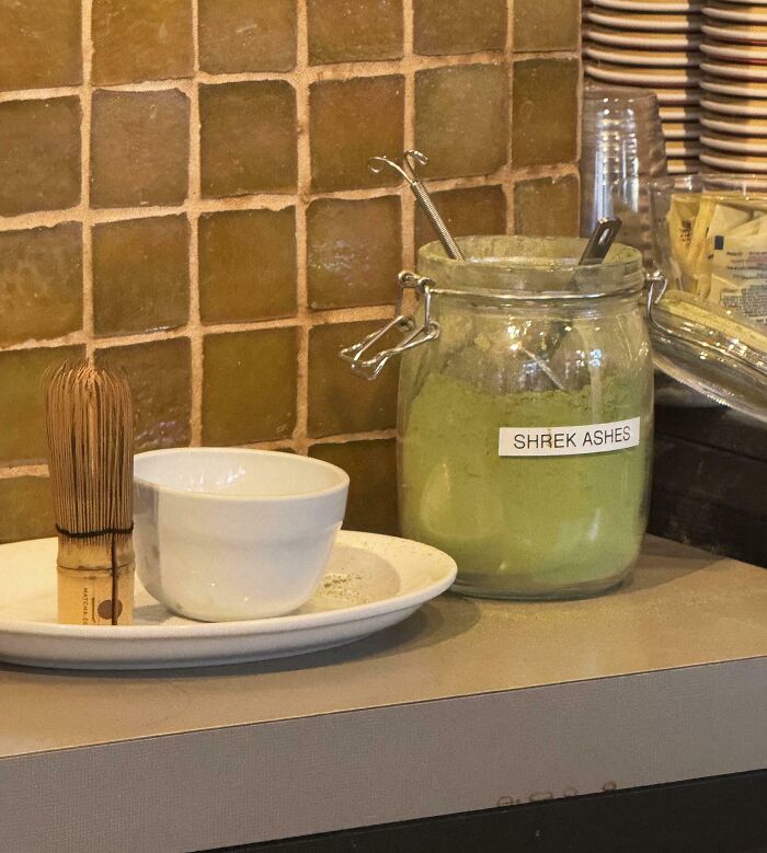 Glass jar labeled Shrek ashes with tea whisk and cup on a plate, capturing funny pictures from 2025 weirdness.