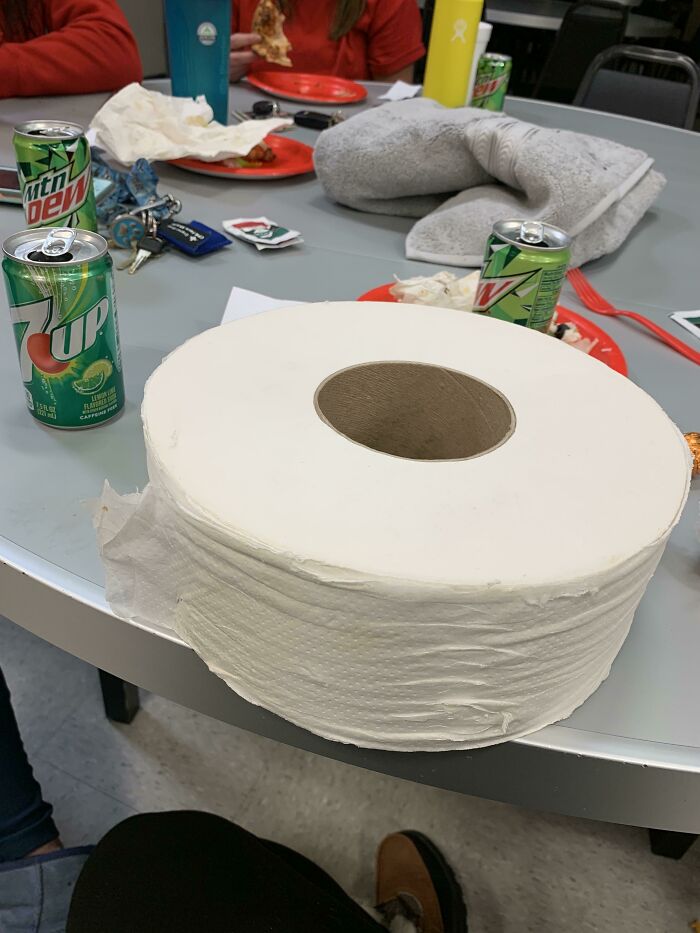 Large roll of toilet paper on a table surrounded by soda cans and food, one of the hilariously bad Secret Santa gifts.