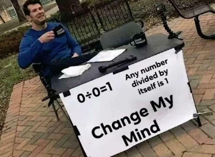 Man sitting at outdoor table with sign challenging math problem about division and numbers, weirdest math problems theme.