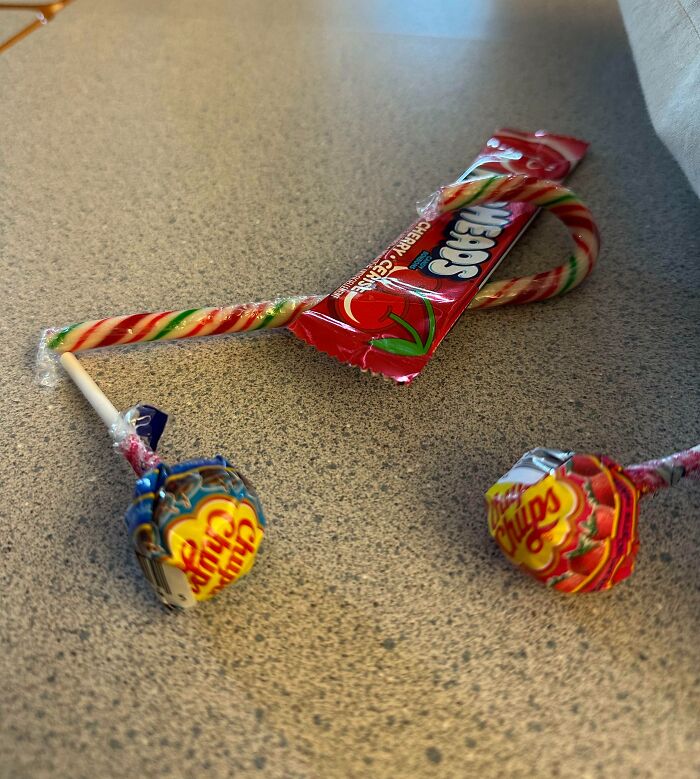 Candy assortment including two Chupa Chups lollipops, a candy cane, and a Cherry Sours, example of bad Secret Santa gifts.