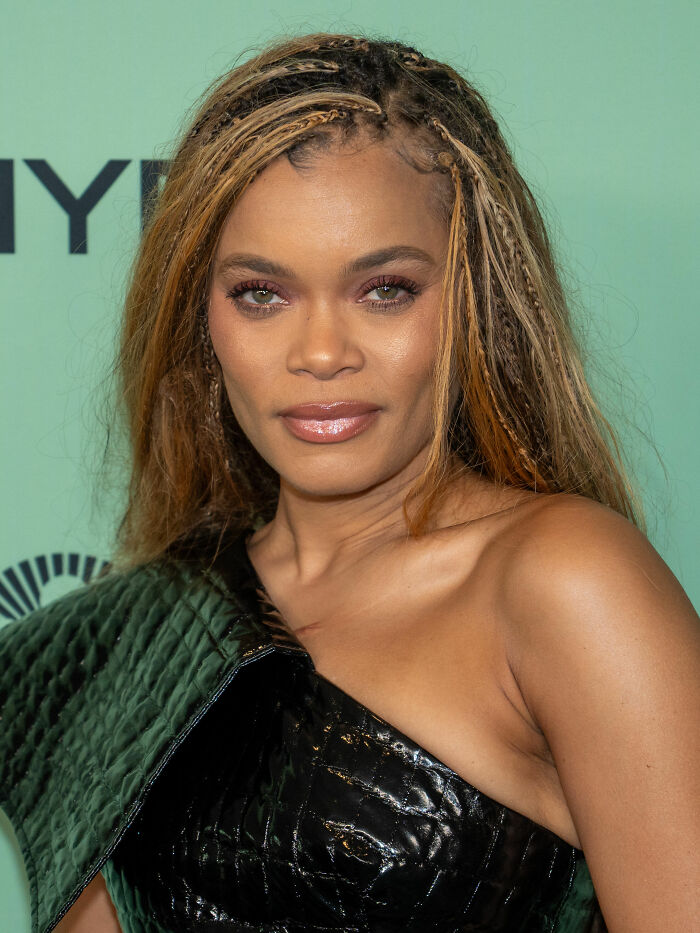Andra Day with braided hair and glossy lips, wearing a black textured one-shoulder outfit at an event.