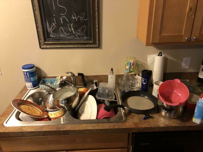Kitchen sink filled with dirty dishes and utensils, illustrating entitled person clutter and lack of cleanliness in 2025 context.