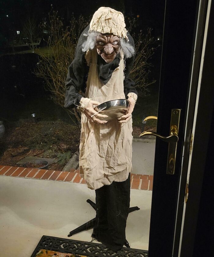 Creepy figure in ragged clothes holding a metal bowl outside a door, one of the funny pictures capturing 2025 weirdness.