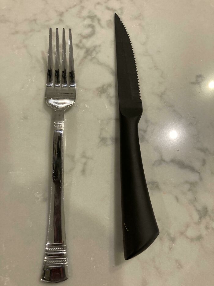 Fork and serrated knife placed side by side on a marble surface illustrating the contrast in sibling relationships.