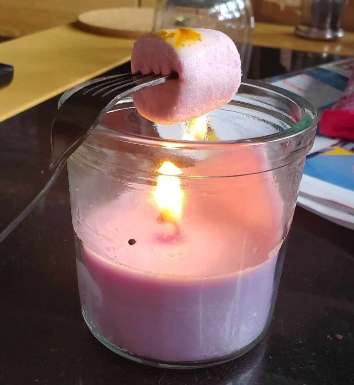 Pink marshmallow roasting over a candle flame in a glass jar, capturing a fun sibling moment at home.