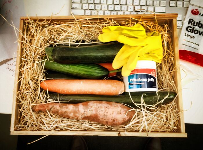 Box of random items including vegetables, yellow gloves, and petroleum jelly as hilariously bad Secret Santa gifts.