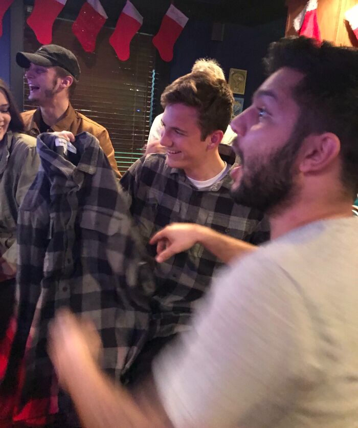 Group of friends laughing and holding a funny, bad Secret Santa gift during a holiday party celebration.