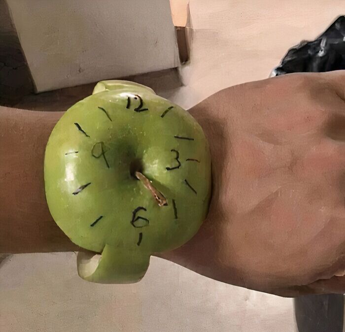 Green apple carved as a watch with clock numbers, worn humorously on a person's wrist in a random funny pic.