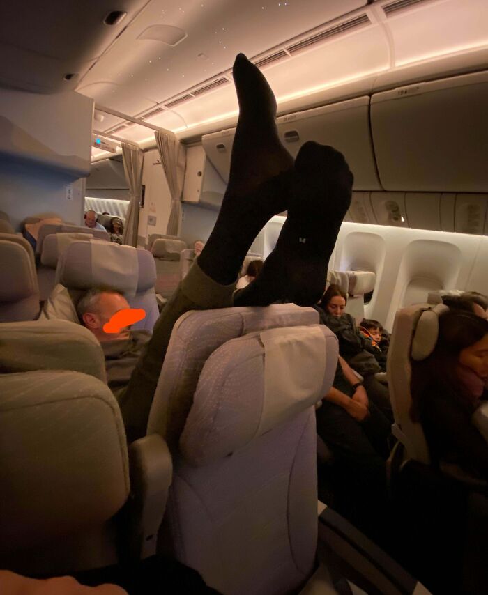 Passenger putting feet on plane seat headrest in socks, rude behavior illustrating next-level jerks