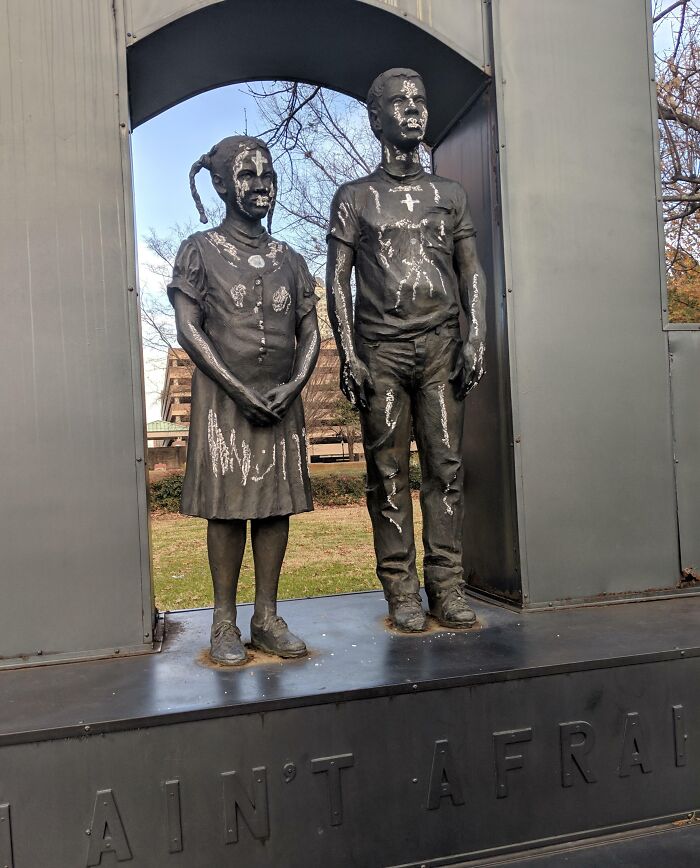 Two vandalized bronze child statues with white paint under metal arch, example of next-level jerks