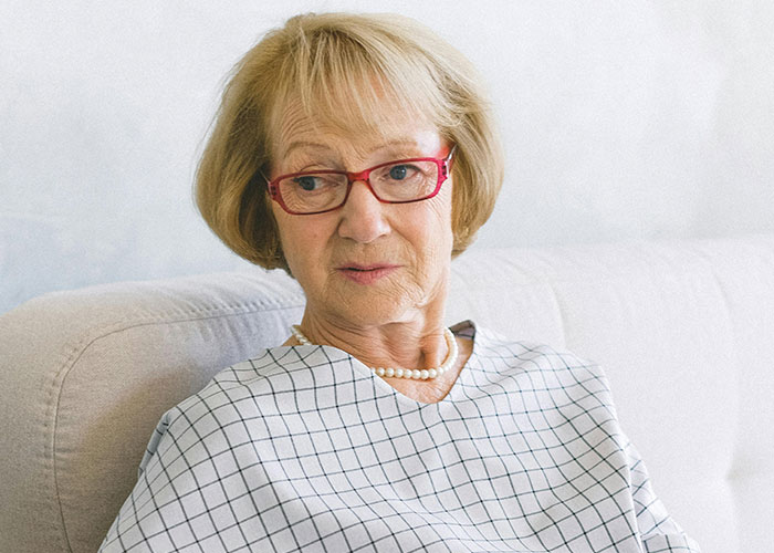 Older woman with red glasses and pearl necklace sitting on a sofa, reflecting on unhinged things her MIL said.