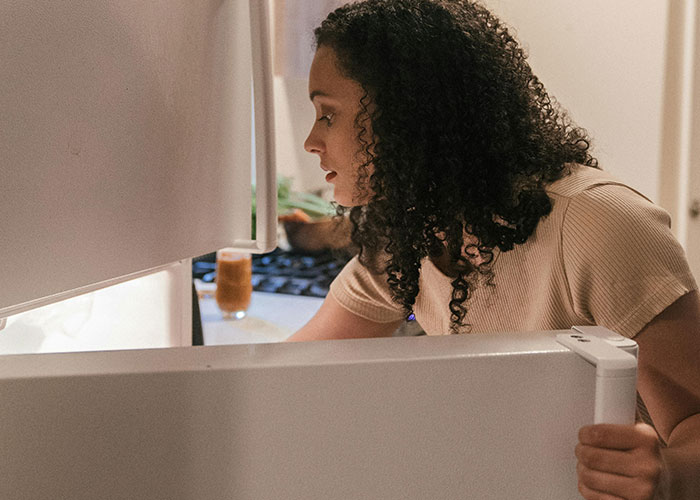 Woman with curly hair opening the refrigerator in a kitchen, illustrating people sharing insane ex stories.