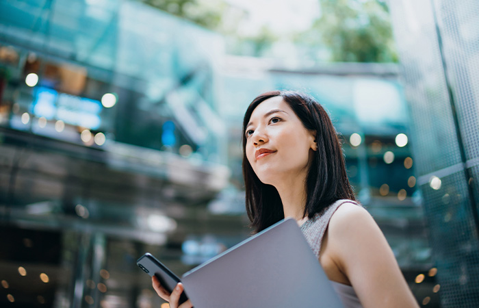 Young woman holding laptop and phone outdoors, representing confidence and traits men find attractive in women.