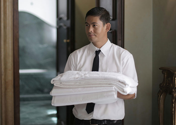 Man working in luxury industry holding fresh towels and linens in an upscale setting showing things the rich pay for that are rip-offs