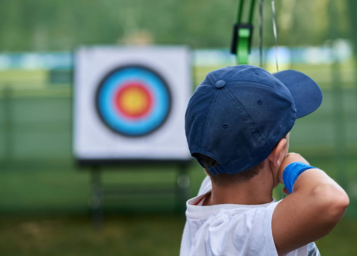 Child wearing a navy cap aiming at an archery target, capturing the moment people start to question what they really saw.