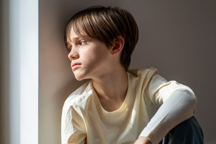 Boy with serious expression staring out window, illustrating next-level evil kids concept for SEO focus.